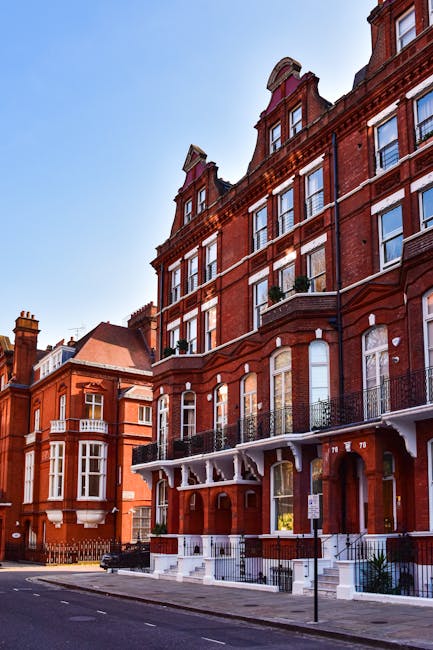 Black and white image of a multi-storey residential building with numerous windows and balconies. The building features a combination of brick and plaster exterior surfaces, and the windows are evenly